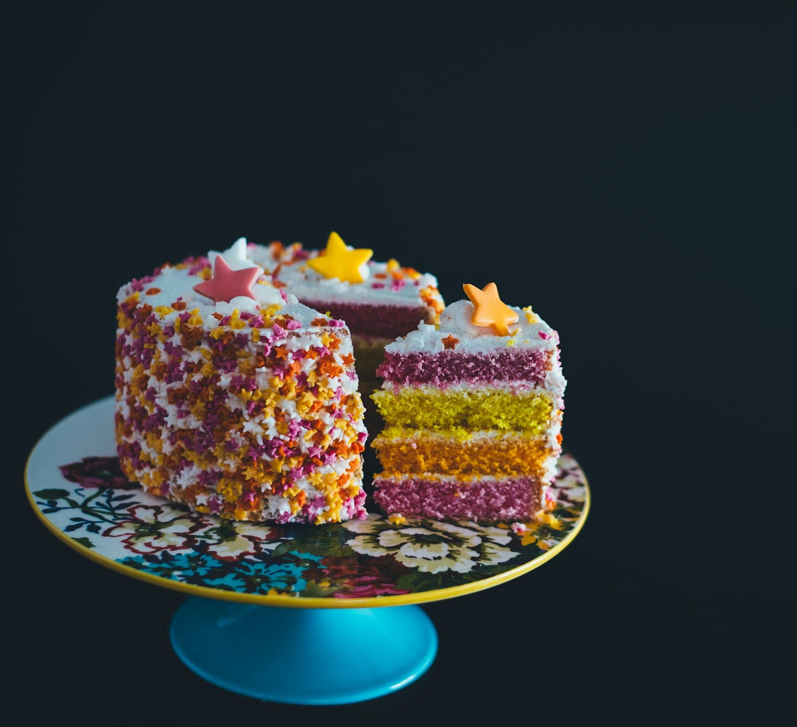 Gâteau d'anniversaire multicolore aux étoiles en sucre, découpé sur un présentoir fleuri