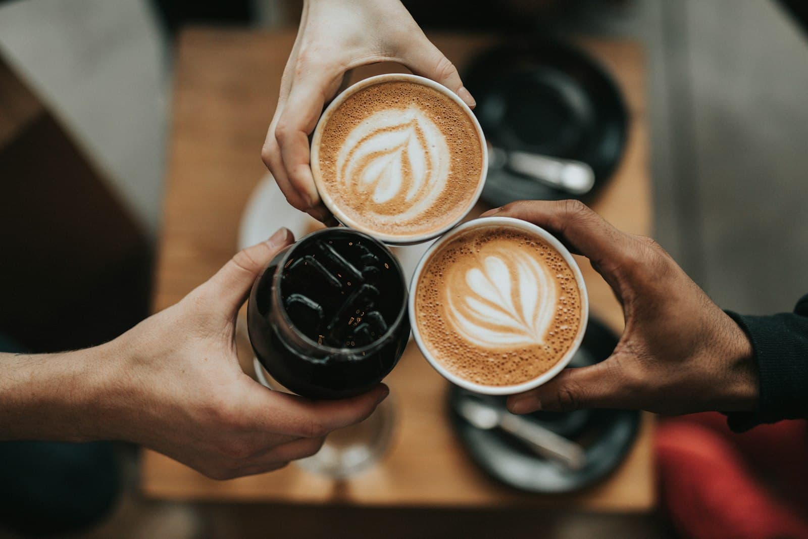 Trois tasses de café levées pour trinquer au-dessus d'une table en bois