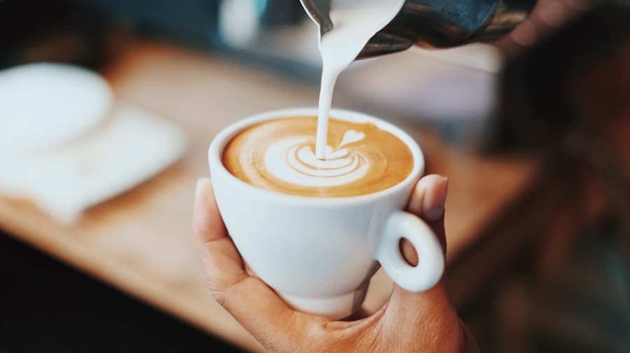 Lait versé en rosette dans une tasse de capucin tenue à la main