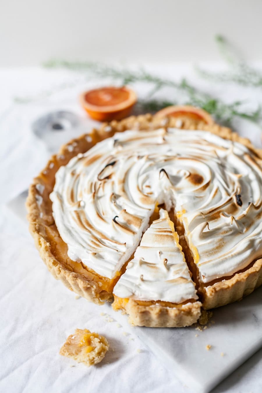 Tarte au citron entiere couverte de meringue flambee, agrumes en arriere-plan